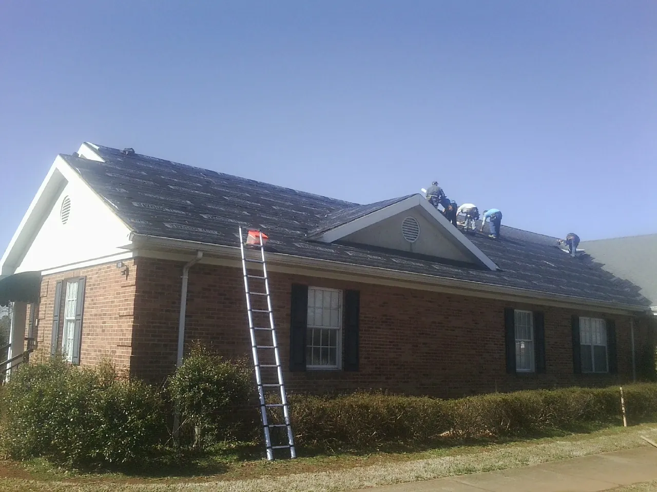 Crew tearing shingles off a brick ranch roof with a ladder set — Emergency Roof Repair work by our crew in Chiloquin