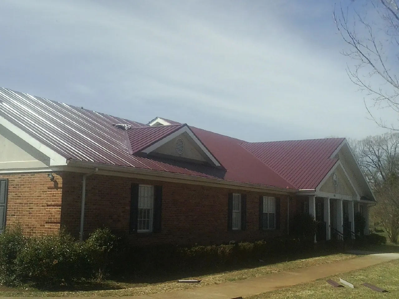 Red metal roof with gabled entries on a long brick building, from a Hail Damage Roof Repair job in Chiloquin