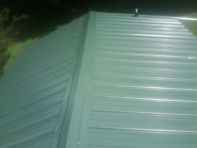 New green metal panels meeting at the ridge of a roof — Flat Roof Repair work by our crew in Chiloquin