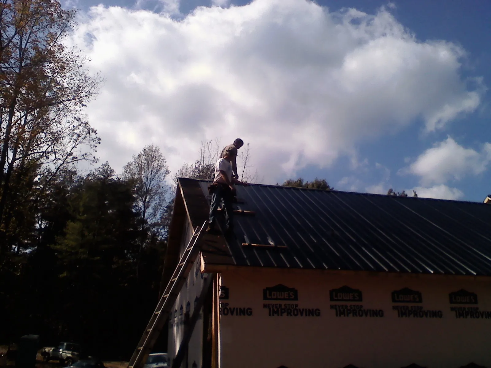 Roofer fastening dark metal panels high against a cloudy sky, from a Roof Inspection job in Chiloquin